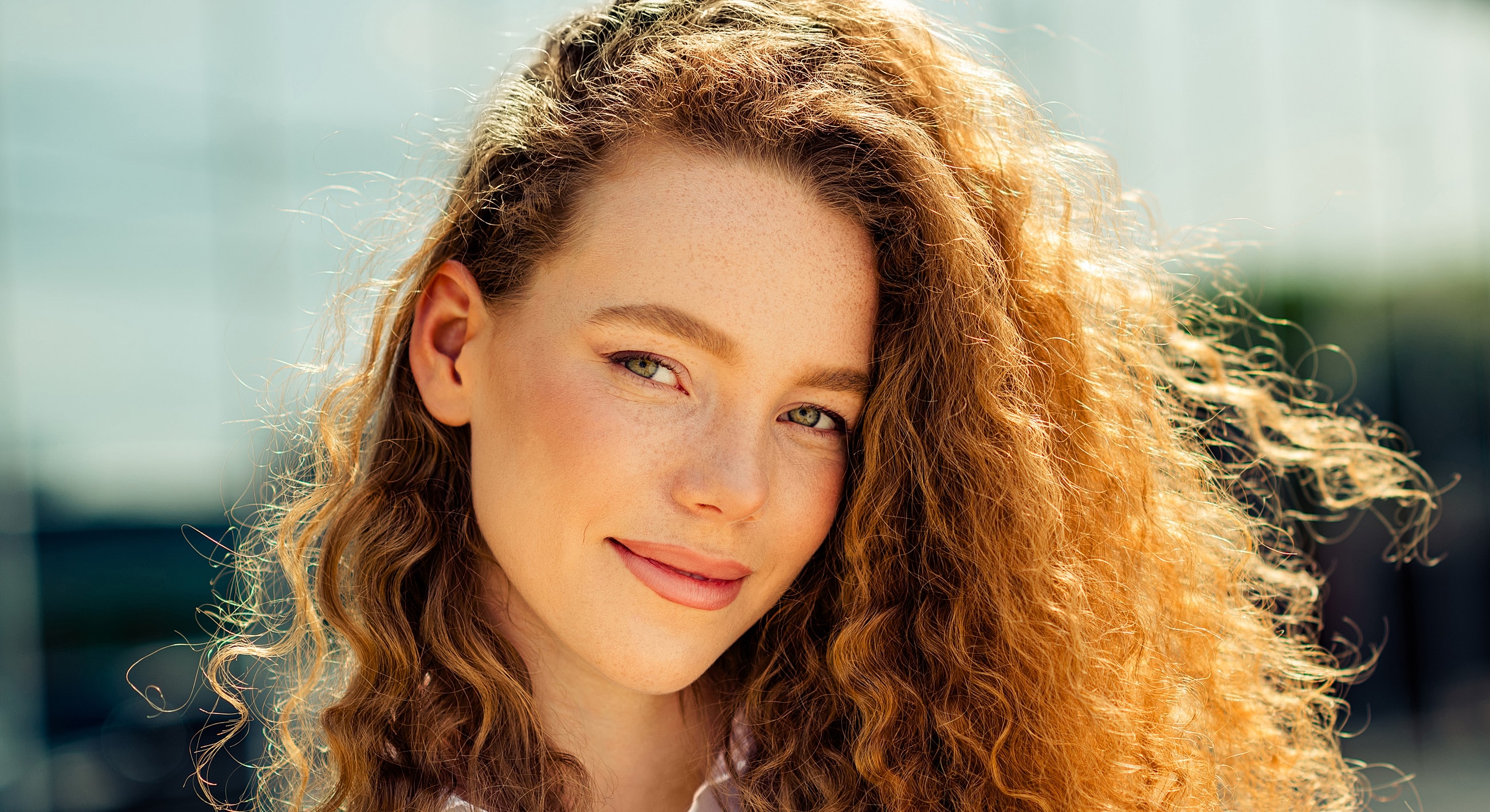 Young woman with curly hair smiling outdoors.