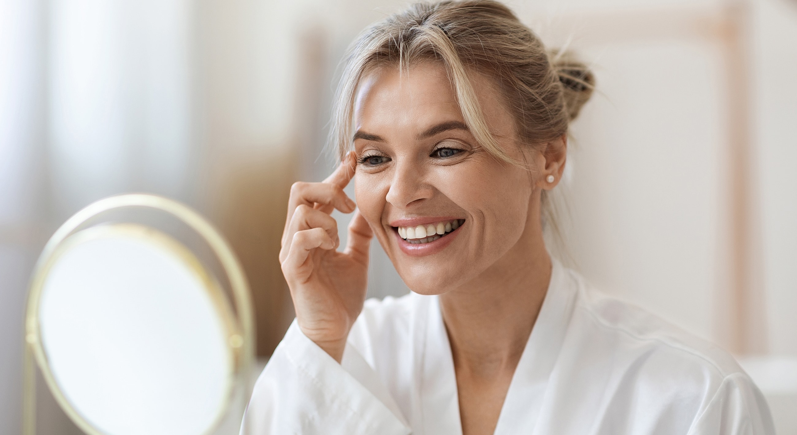 Woman applying skincare while smiling in mirror.